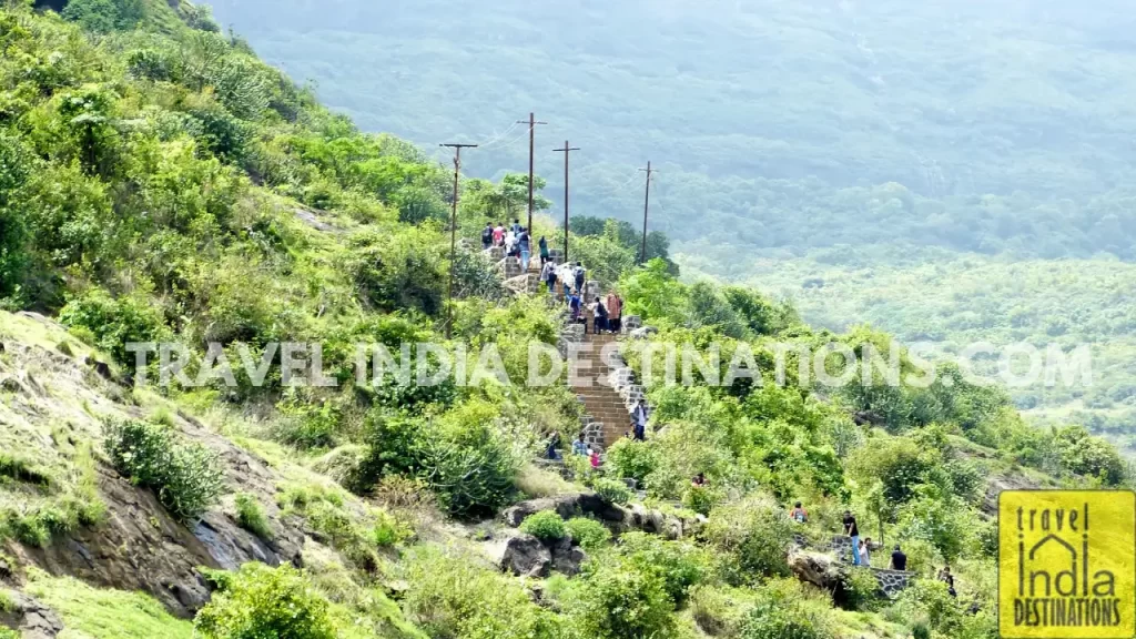 View from the base of the steps leading to Bhaja Caves, with people climbing the winding staircase through the hills.