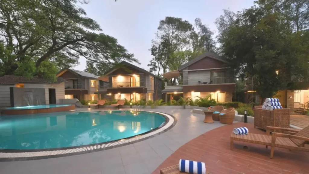 Arova Woods by the Fern Lonavala – wooden cabin-style hotel surrounded by greenery and outdoor swimming pool and sun loungers.