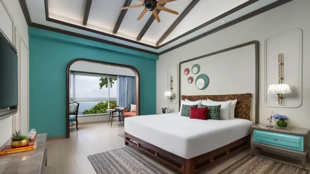 King-size bed at Fountain IHCL Mahabaleshwar with pastel teal wall and balcony seating overlooking the landscape one of the best hotels in Mahabaleshwar
