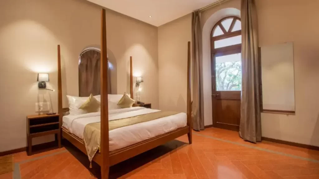 Bedroom at RR Heritage Resort Mahabaleshwar with four-poster bed, warm tones, and full-length curtains by balcony