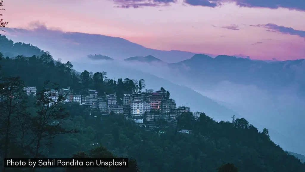 A shot of Gangtok Sikkim with misty mountains and lush greenery and pink sunset sky ideal for honeymoon in February in India.
