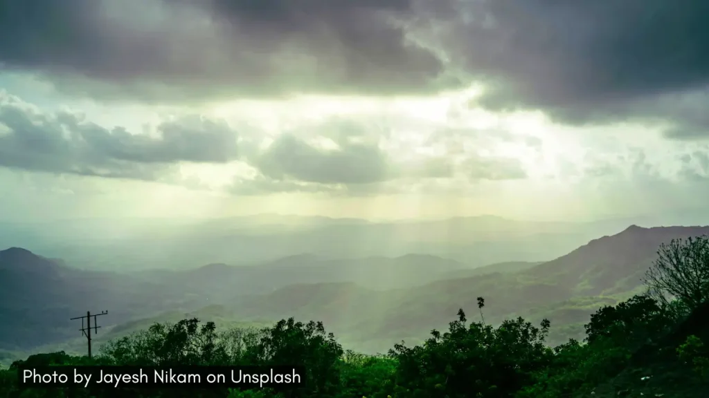 A panoramic view of the Amboli Ghat in Maharashtra with sun rays penetrating through dark monsoon clouds.