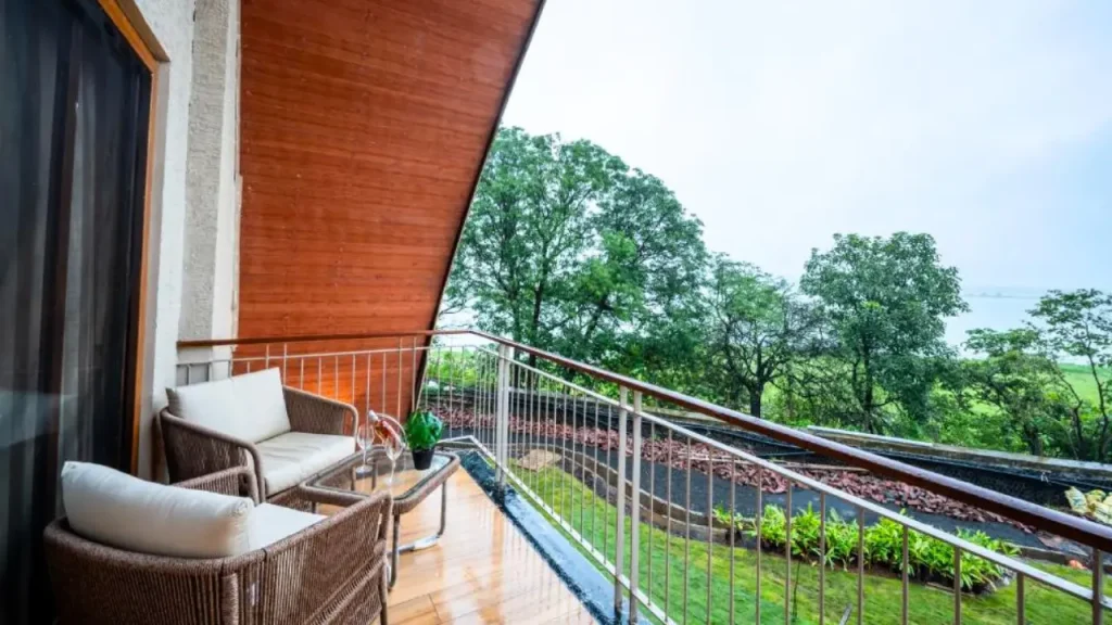 Balcony area of ARK Lake Resort Deluxe Room overlooking the landscaped garden and lake beyond it, one of the best wellness retreats in Igatpuri.