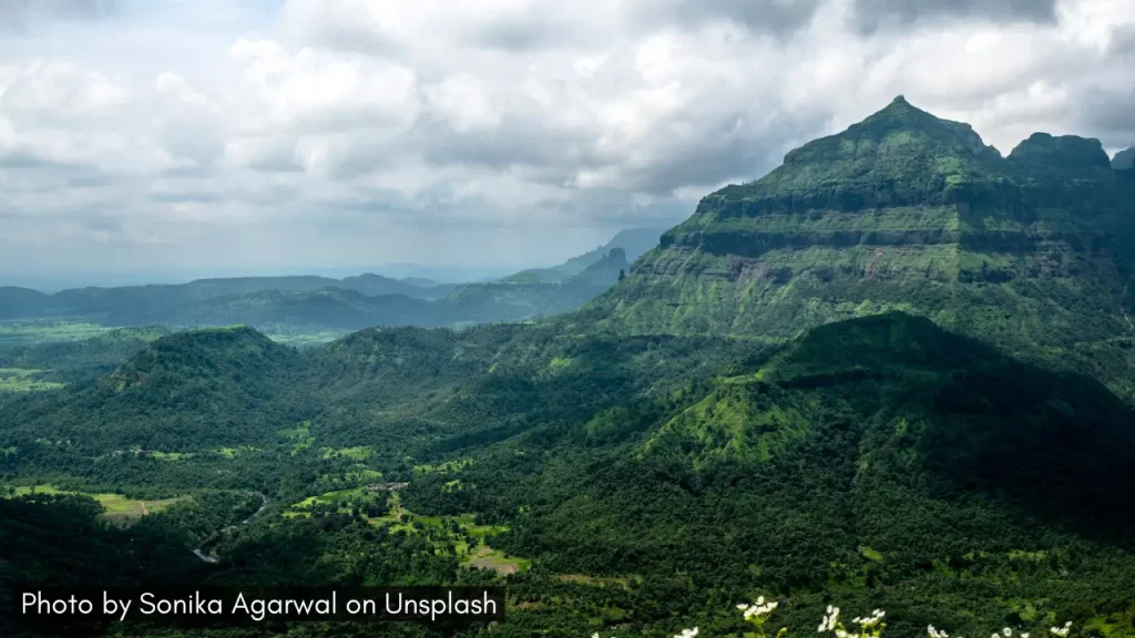 A panoramic shot of the Malshej Ghat in Maharashtra with monsoon clouds hovering and lush green landscape.