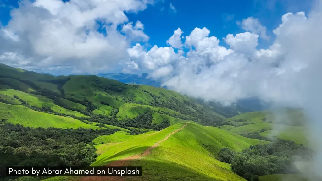 Stunning views of the lush green hills in Chikmagalur covered with misty white clouds hovering the blue sky.